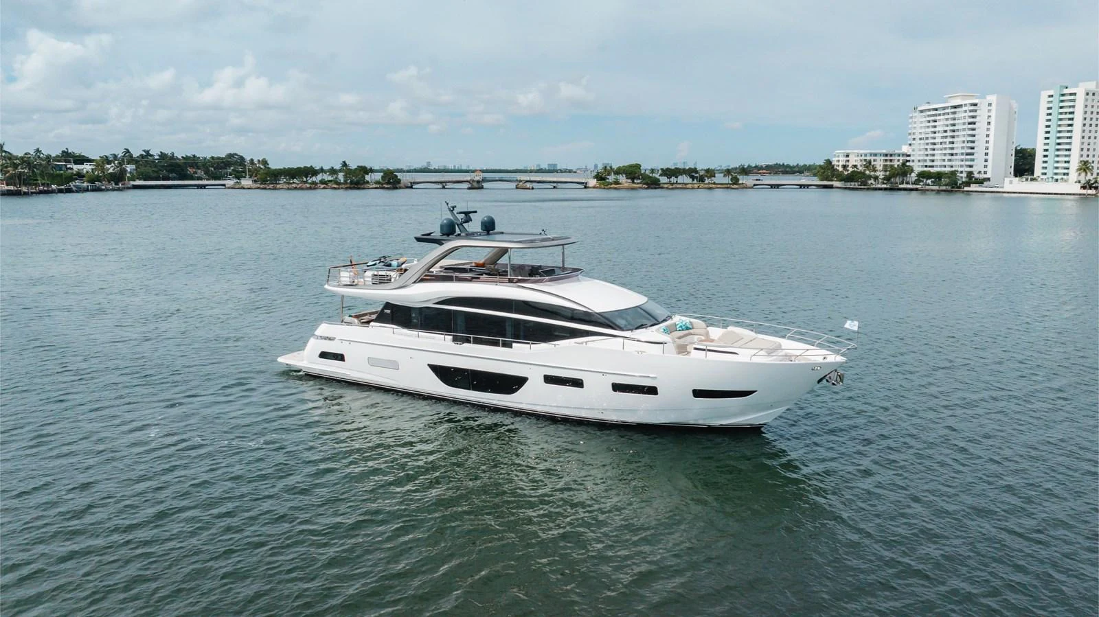 A sleek and modern yacht cruising on calm waters with a cityscape in the background. aboard TOMORROW NEVER KNOWS Yacht for Sale