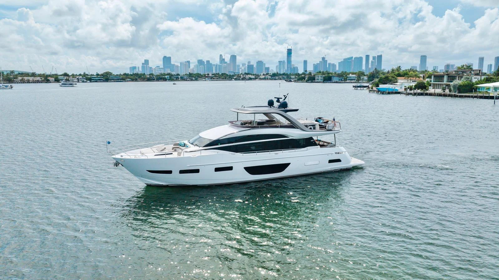 A sleek and modern yacht glides gracefully on calm waters with a city skyline in the background. aboard TOMORROW NEVER KNOWS Yacht for Sale