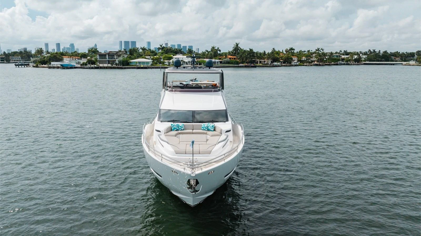 A sleek yacht is anchored on calm waters with a cityscape in the background. aboard TOMORROW NEVER KNOWS Yacht for Sale