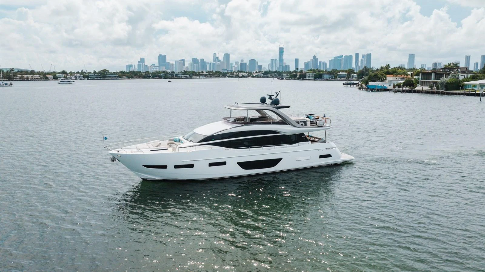 A sleek and modern yacht cruises gracefully on calm waters with a city skyline in the background. aboard TOMORROW NEVER KNOWS Yacht for Sale