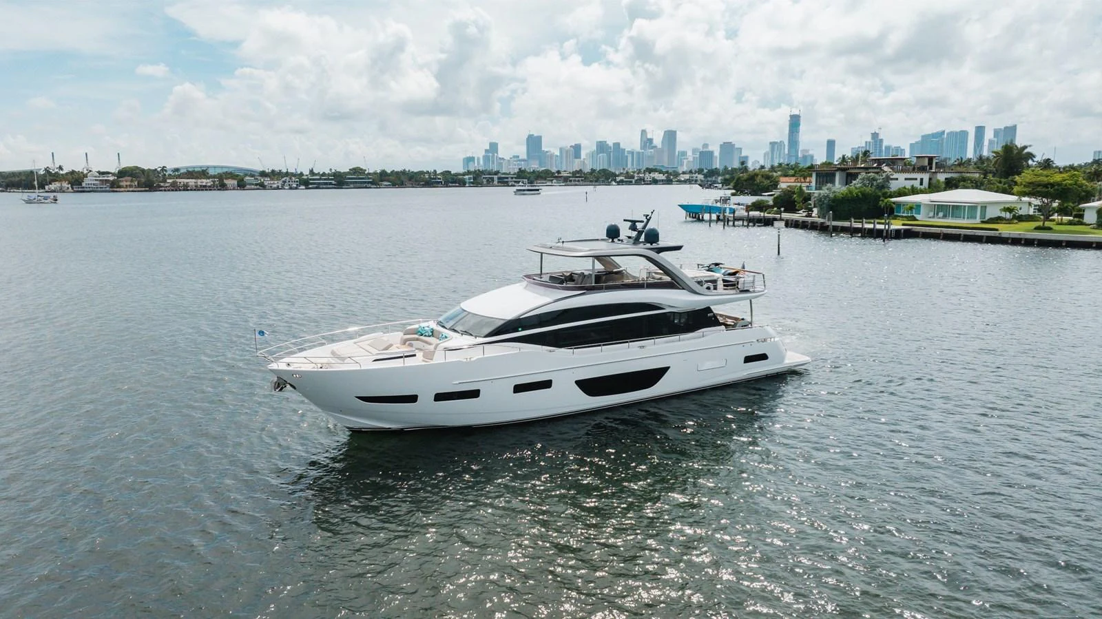 A sleek, modern yacht cruises gracefully on calm waters with a city skyline in the background. aboard TOMORROW NEVER KNOWS Yacht for Sale