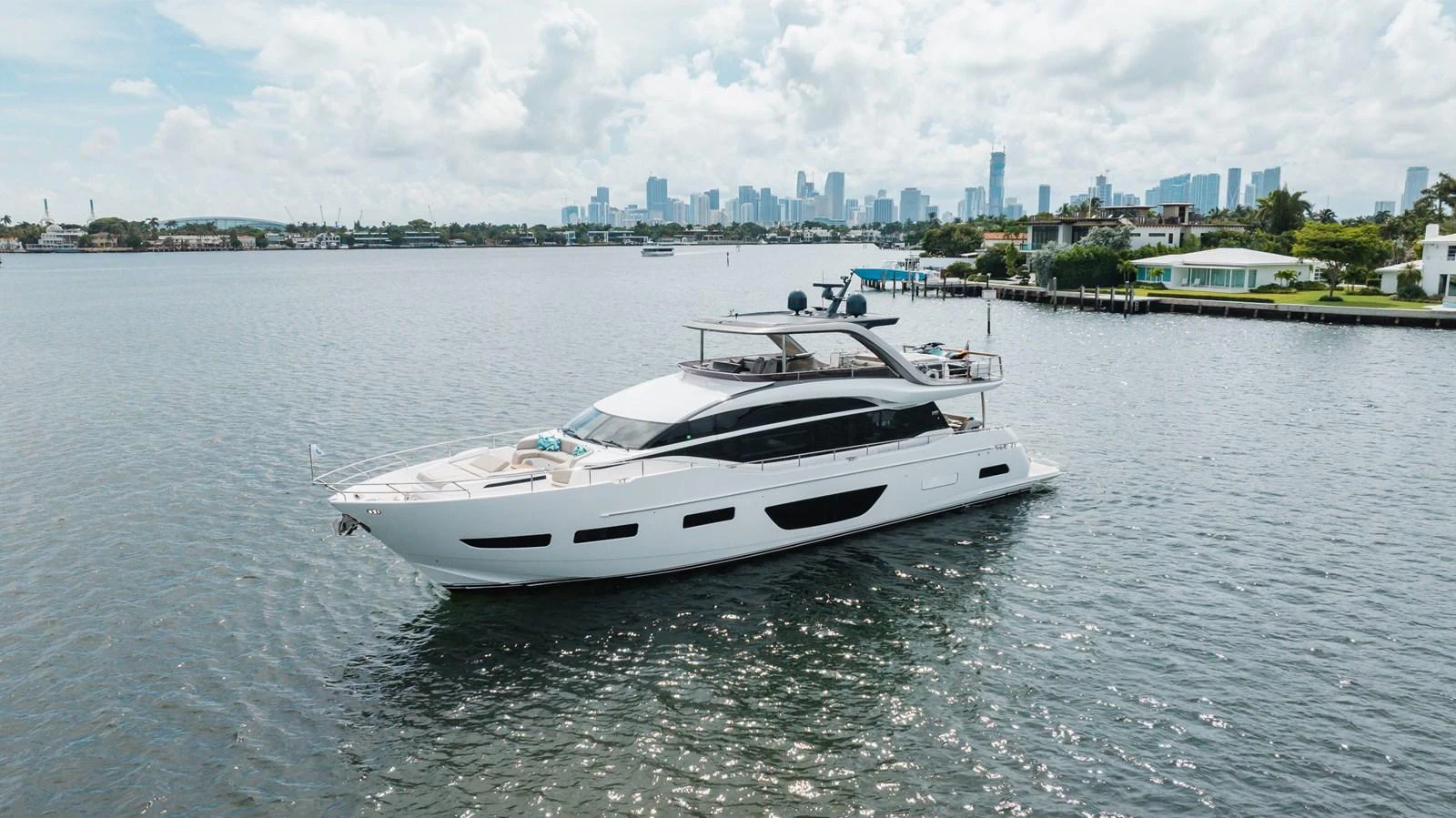 A sleek and modern yacht cruises gracefully on calm waters with a city skyline in the background. aboard TOMORROW NEVER KNOWS Yacht for Sale