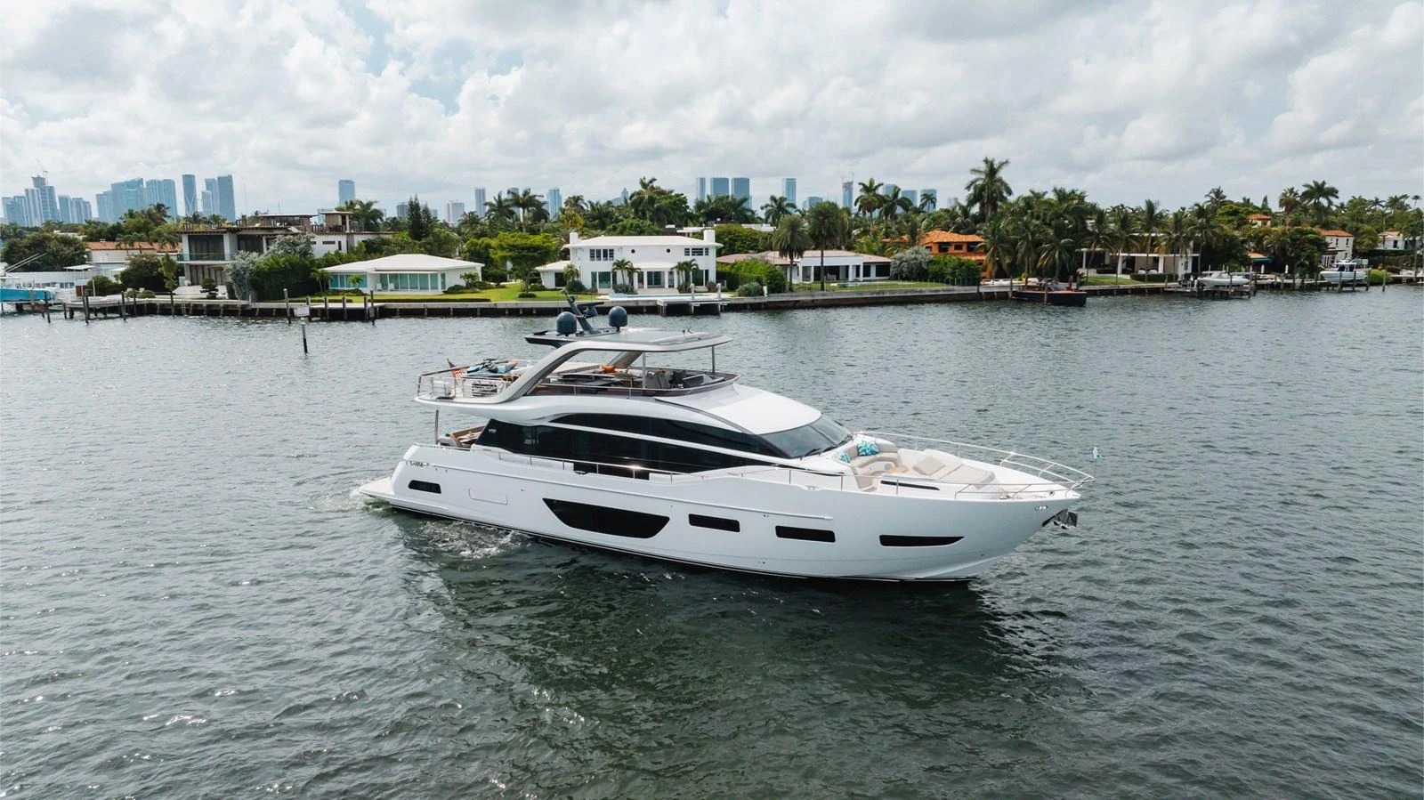 A sleek and modern yacht cruising near a coastal residential area. aboard TOMORROW NEVER KNOWS Yacht for Sale