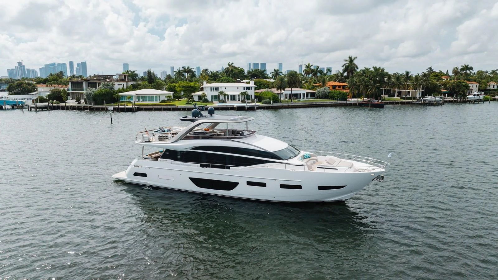 A sleek and modern yacht cruising near a coastal residential area. aboard TOMORROW NEVER KNOWS Yacht for Sale