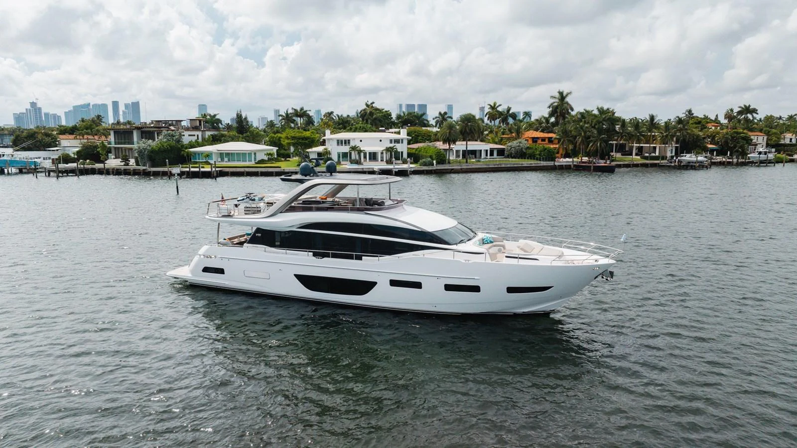 A sleek and modern yacht cruises gracefully on calm waters near a luxurious waterfront neighborhood. aboard TOMORROW NEVER KNOWS Yacht for Sale