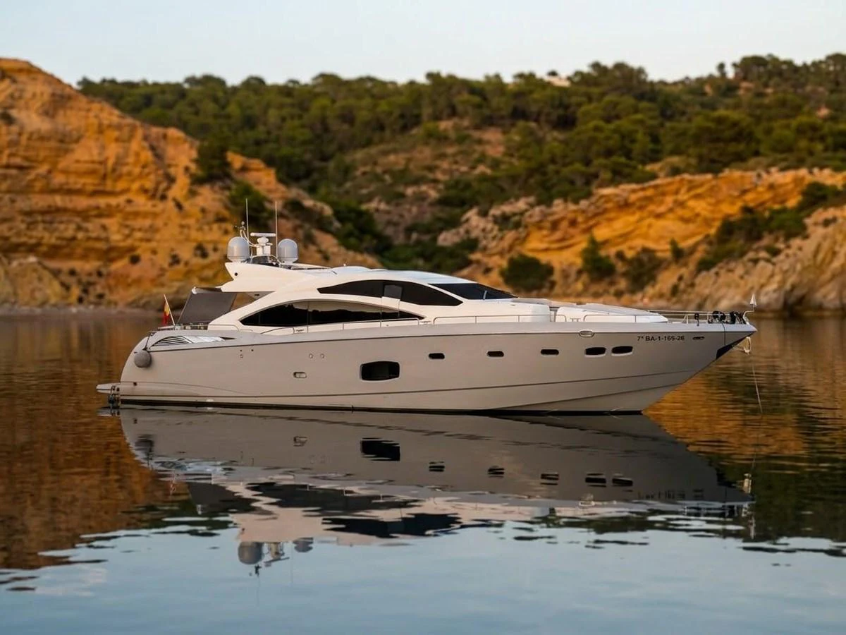 A sleek and modern yacht is anchored in a serene, rocky cove with calm waters reflecting its elegant profile. aboard PELAGIA Yacht for Sale