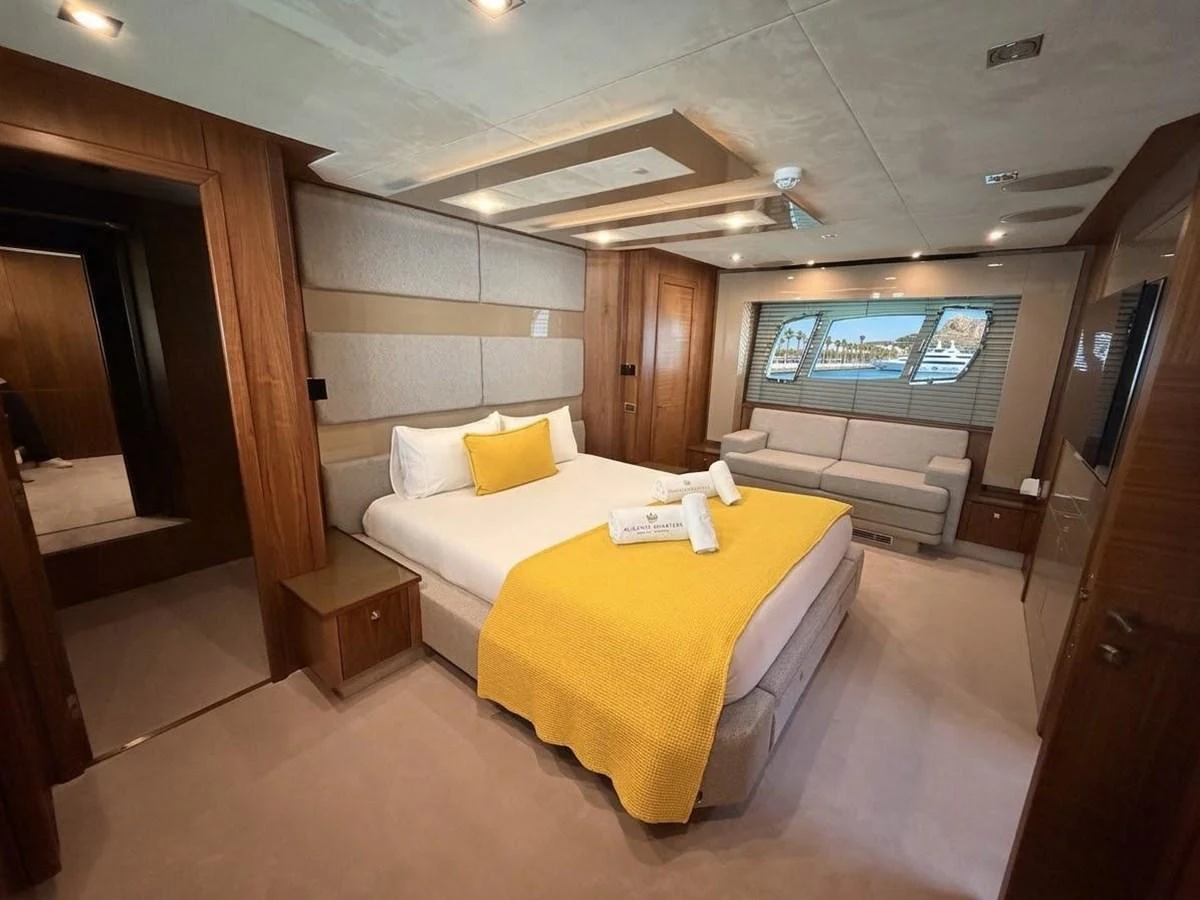 The master stateroom features a luxurious bed with a yellow throw, a comfortable sofa, and elegant wood paneling. aboard PELAGIA Yacht for Sale