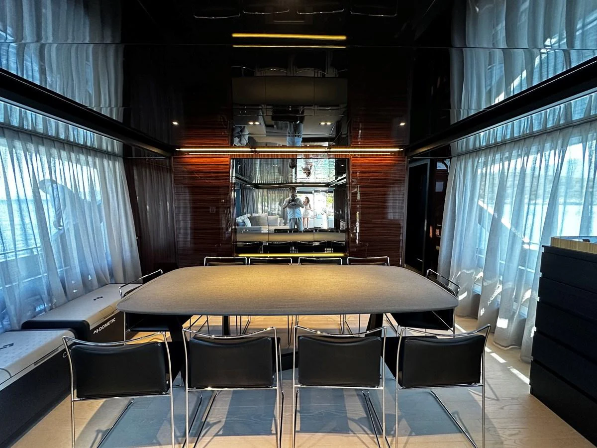 The yacht's dining area features a sleek table with modern chairs, surrounded by large windows draped with sheer curtains. aboard 4SEAS Yacht for Sale