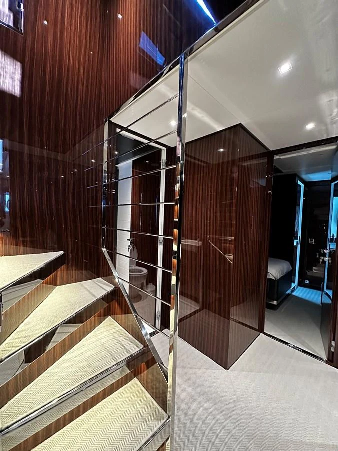 A sleek and modern staircase with polished wood paneling and chrome accents leads to the lower deck. aboard 4SEAS Yacht for Sale