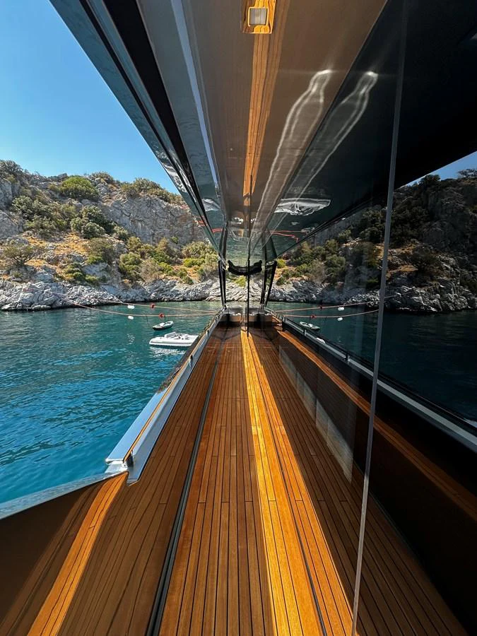 A sleek yacht with a polished deck reflecting the serene waters and rocky coastline. aboard 4SEAS Yacht for Sale