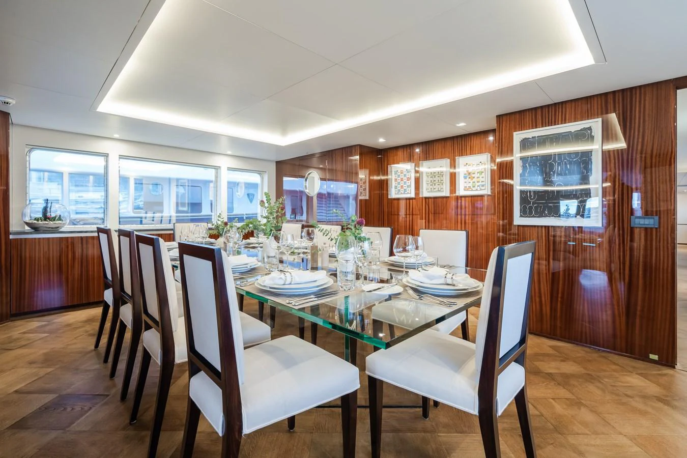 The yacht's dining area features a sleek glass table surrounded by elegant wooden and white upholstered chairs, creating a sophisticated dining experience. aboard MP5 Yacht for Sale