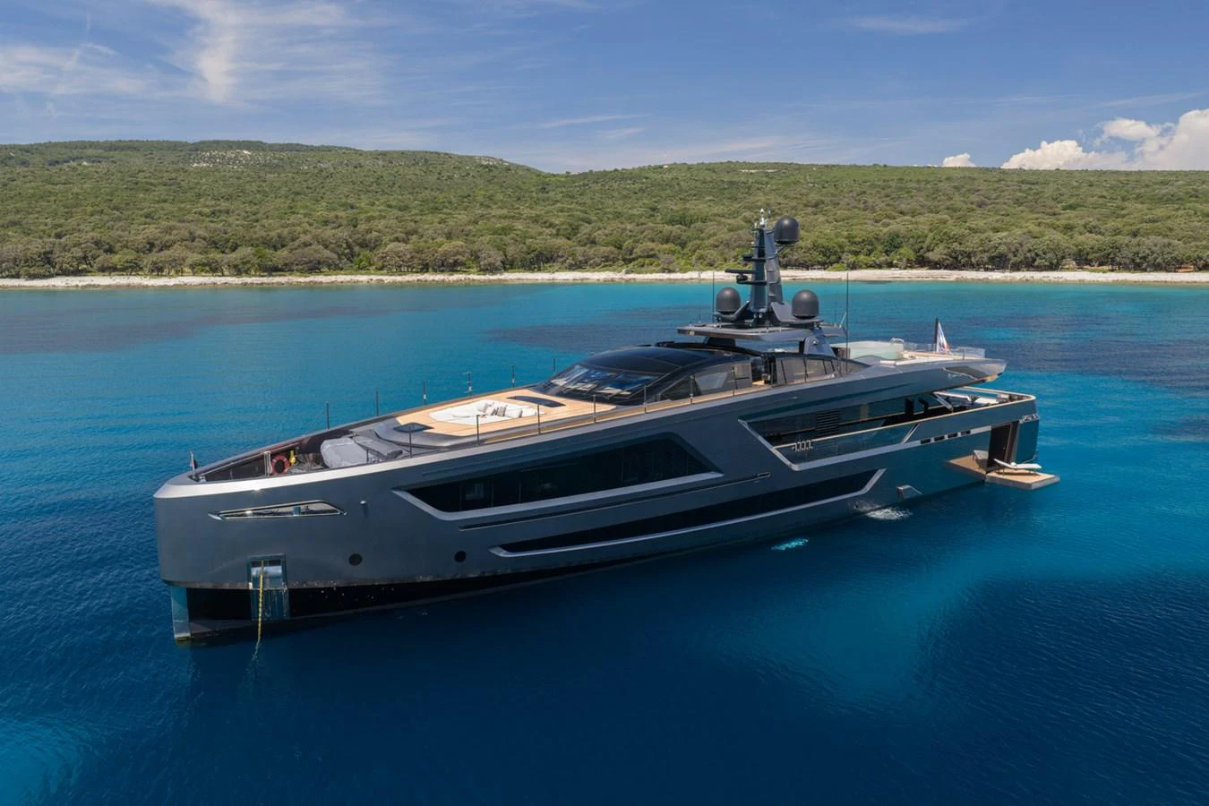 A sleek and modern yacht is anchored in crystal-clear blue waters against a lush green shoreline. aboard PANAM Yacht for Sale