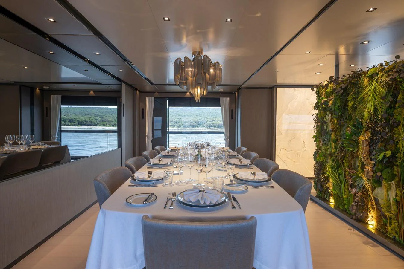 The yacht's dining area features an elegant table setting with a view of the water and a lush vertical garden. aboard PANAM Yacht for Sale