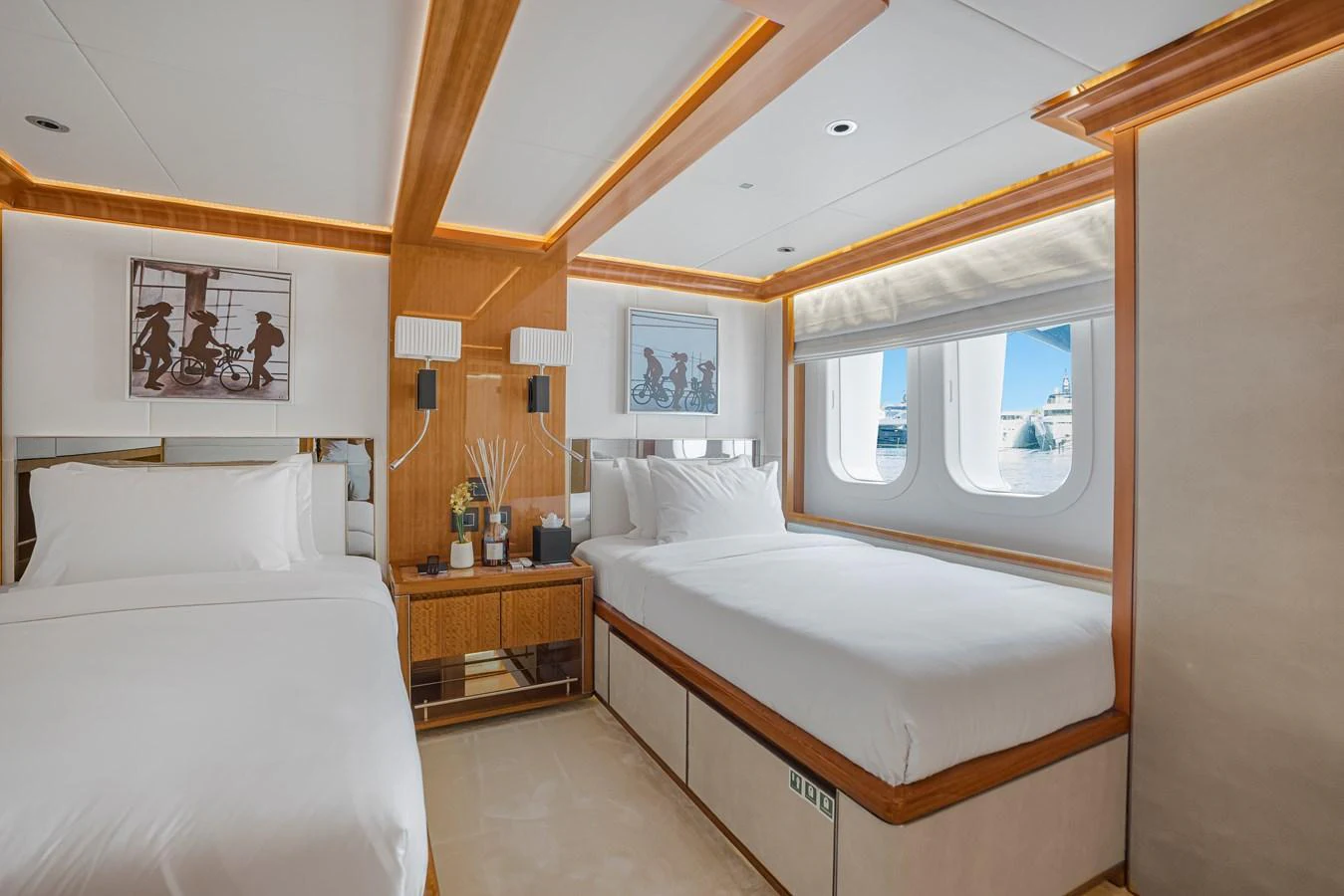The guest stateroom features two comfortable beds with elegant wooden accents and large windows offering a view of the sea. aboard ATLANTIS Yacht for Sale