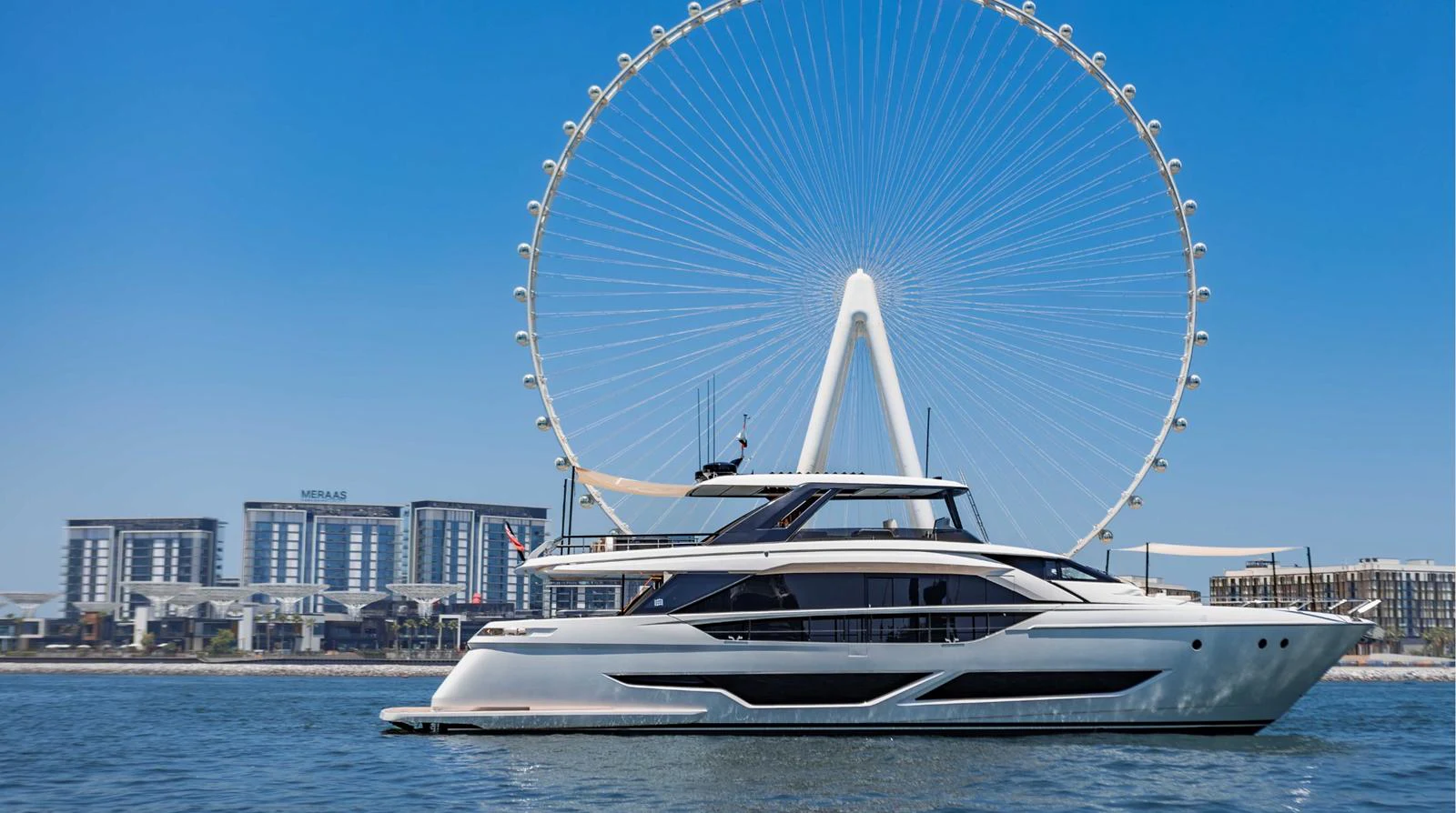 A sleek yacht cruises in front of a giant Ferris wheel on a sunny day. aboard AMANI Yacht for Sale