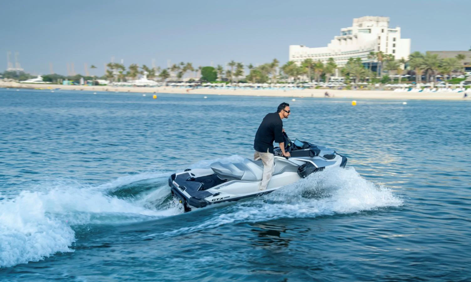 A person enjoys a thrilling ride on a jet ski near a beautiful beach resort. aboard AMANI Yacht for Sale