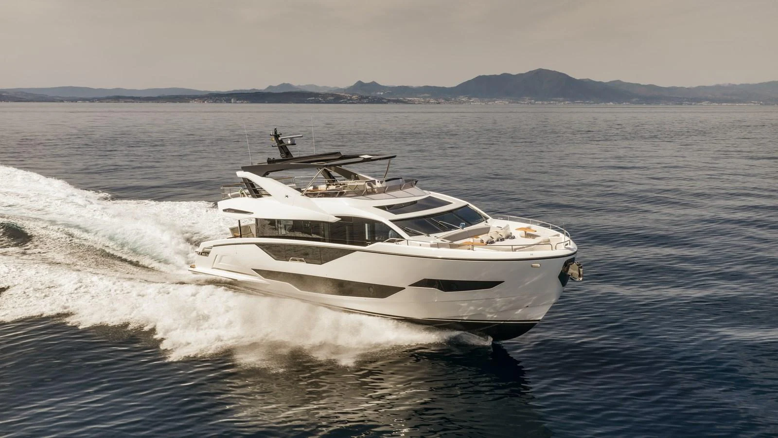 A sleek and modern yacht cruises swiftly across calm waters with a scenic coastline in the background. aboard W OF JERSEY Yacht for Sale