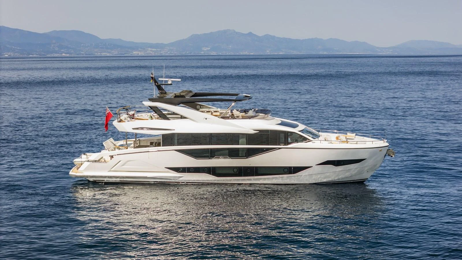 A sleek and modern yacht cruising on calm waters with a scenic mountainous backdrop. aboard W OF JERSEY Yacht for Sale