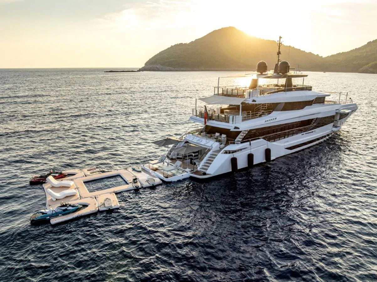 A luxurious yacht anchored in serene waters with a stunning backdrop of hills and a beautiful sunset. aboard TOY Yacht for Sale