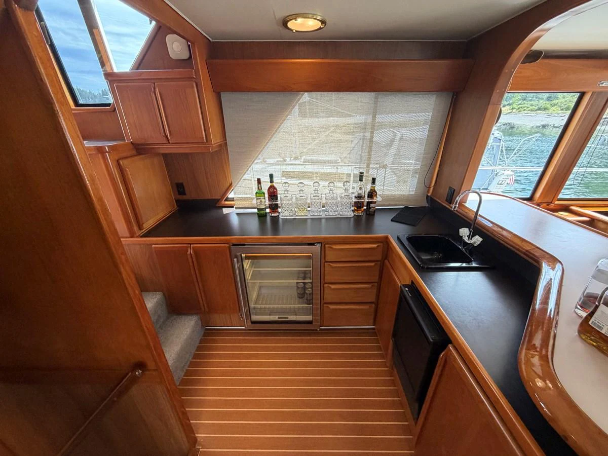 The yacht's galley features sleek wooden cabinetry, a compact refrigerator, and a well-organized countertop with a sink. aboard OCEAN PACIFIC Yacht for Sale