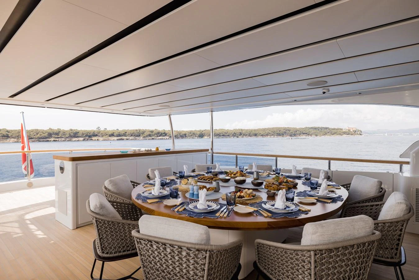 The aft deck features an elegant dining area with a large round table set for a meal, offering stunning views of the water. aboard ADVA Yacht for Sale