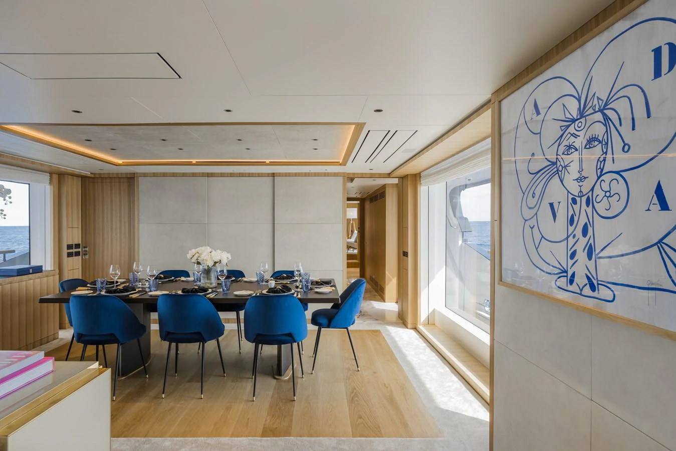 The yacht's dining area features a modern design with elegant blue chairs and a large window providing a stunning sea view. aboard ADVA Yacht for Sale