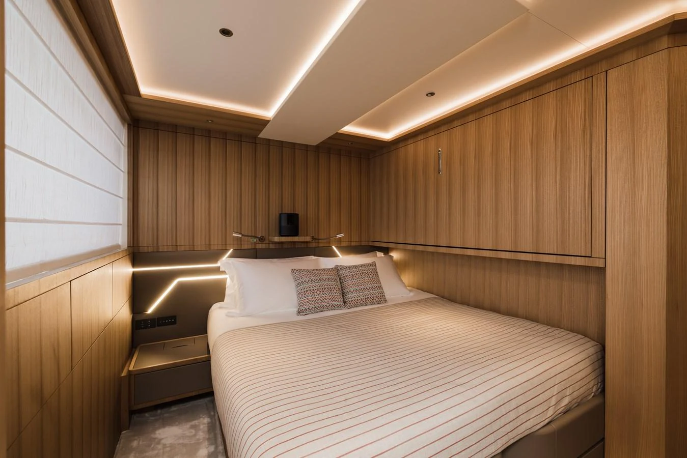 The stateroom features a cozy bed with elegant wood paneling and ambient lighting. aboard ADVA Yacht for Sale