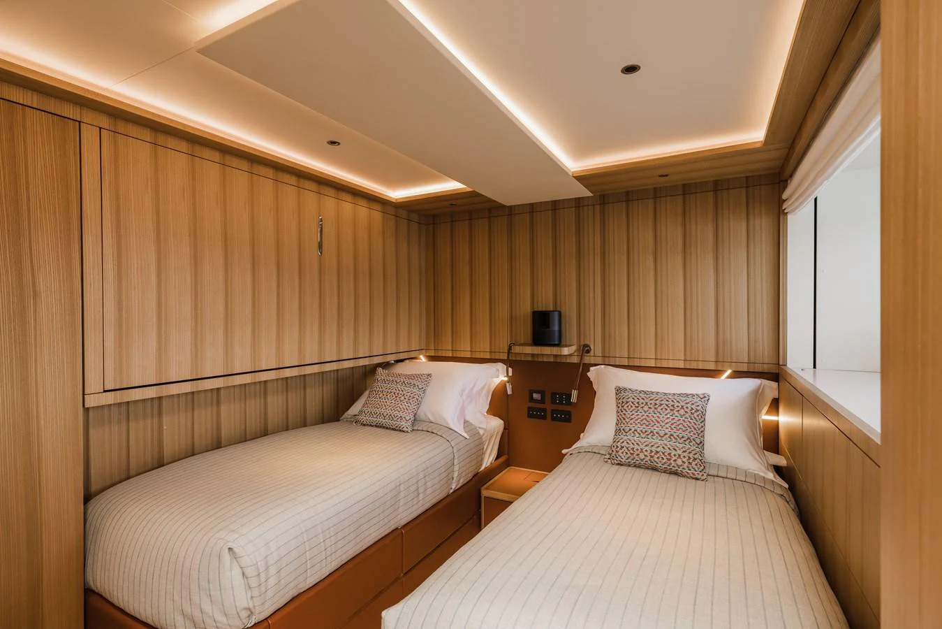 The twin stateroom features two single beds with modern wood paneling and ambient lighting. aboard ADVA Yacht for Sale