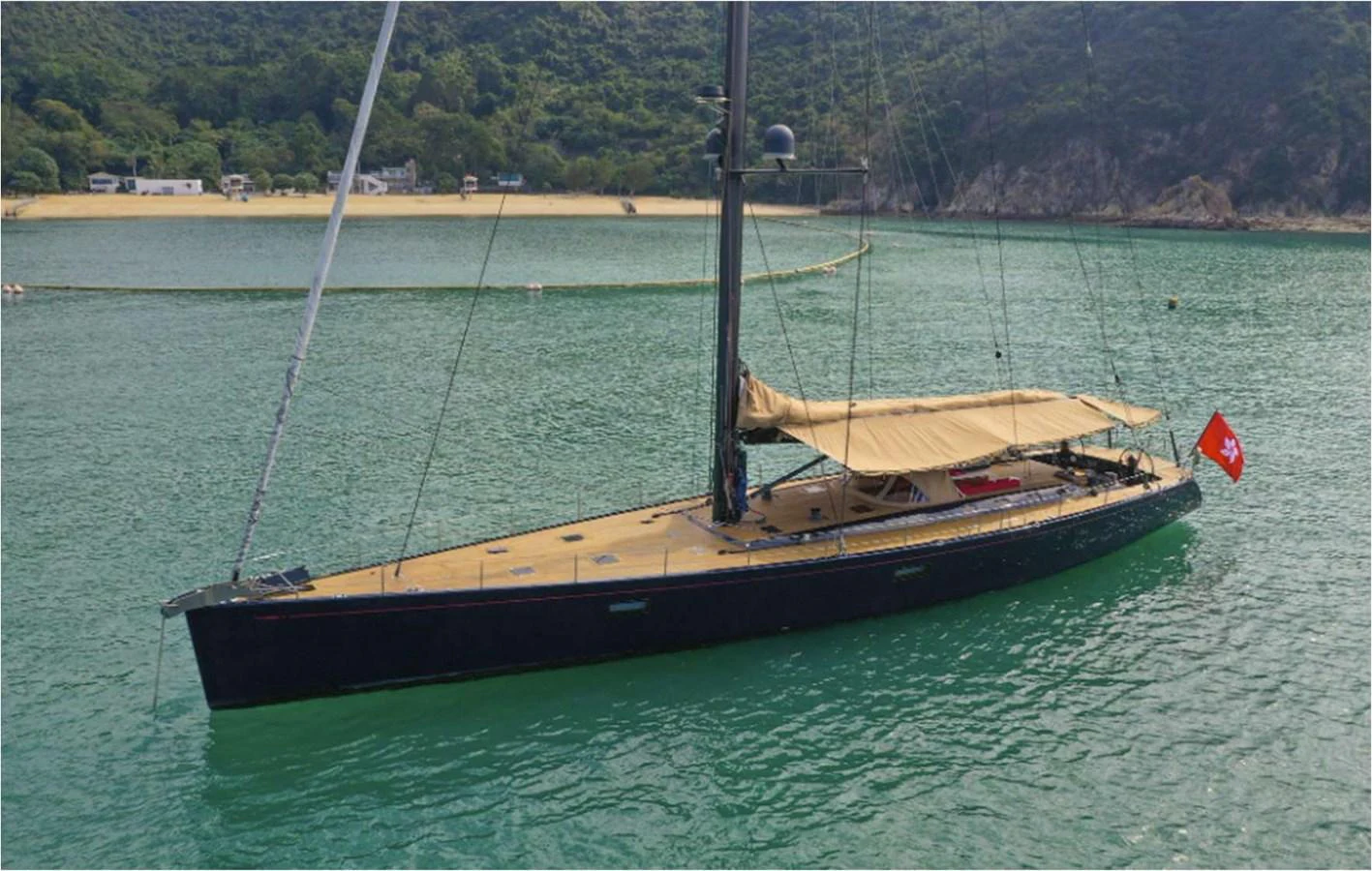 A sleek sailing yacht with a dark hull and tan deck is anchored in a serene bay. aboard NAUTOR SWAN 90 Yacht for Sale