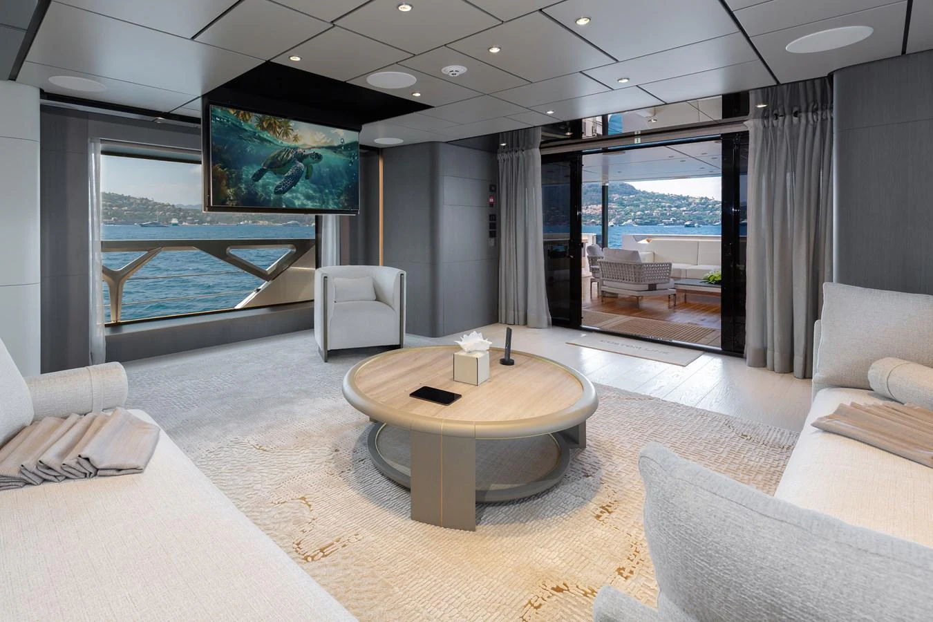 The salon features plush seating, a round coffee table, and a large TV, with a view of the sea through expansive windows. aboard LADY DIA Yacht for Sale