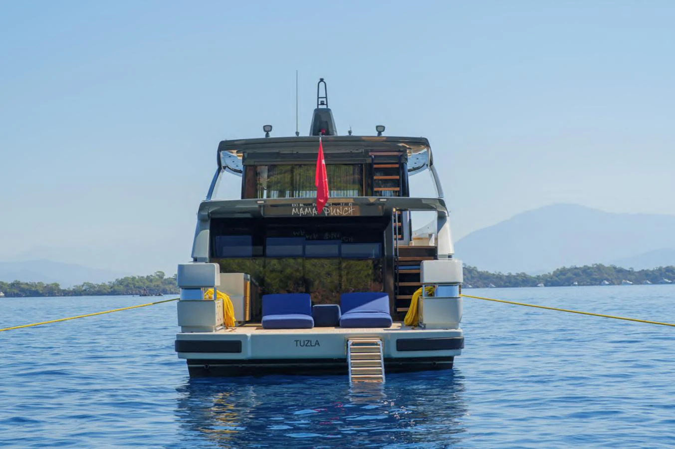 The yacht is anchored in calm waters, showcasing its inviting aft deck with comfortable seating and a swim platform. aboard OUT OF THE BLUE Yacht for Sale