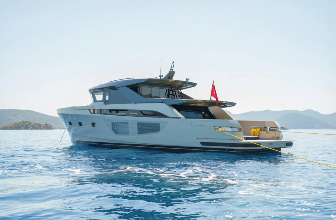 A sleek yacht is anchored in calm blue waters with scenic hills in the background. aboard OUT OF THE BLUE Yacht for Sale