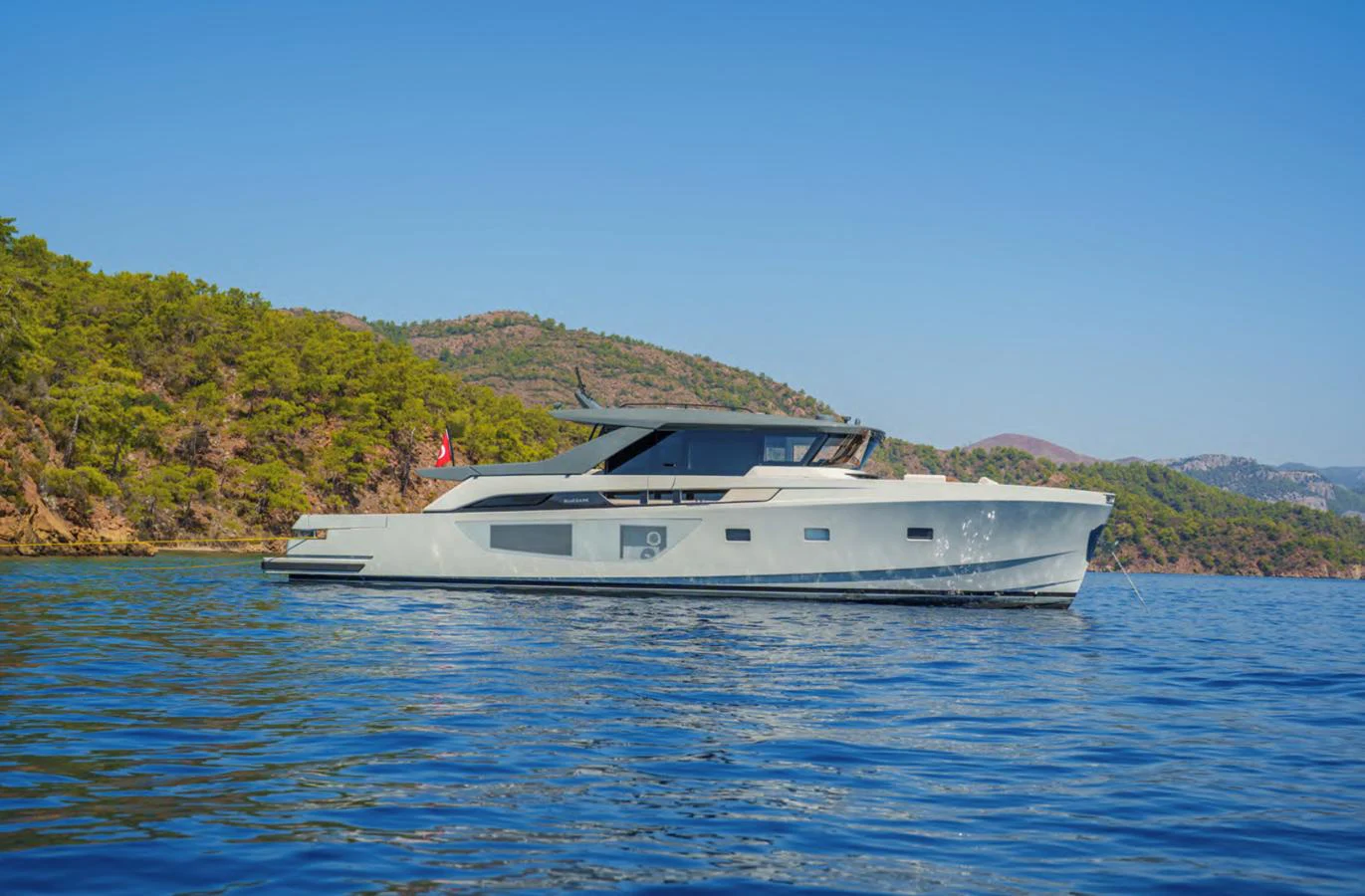 A sleek, modern yacht glides gracefully on calm waters against a backdrop of lush, green hills. aboard OUT OF THE BLUE Yacht for Sale