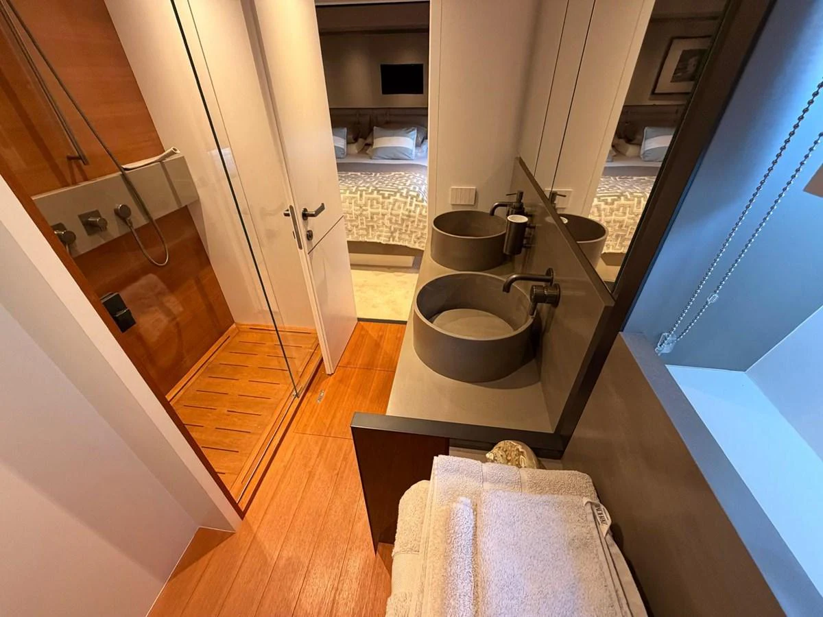 A modern yacht bathroom featuring dual sinks, a glass-enclosed shower, and luxurious wooden flooring. aboard OUT OF THE BLUE Yacht for Sale
