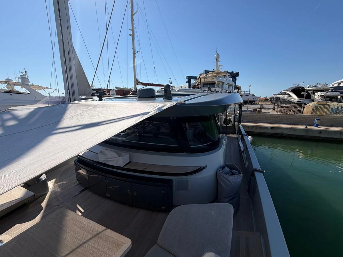 The yacht is docked at a marina, showcasing its sleek design and spacious deck area under a clear sky. aboard OUT OF THE BLUE Yacht for Sale