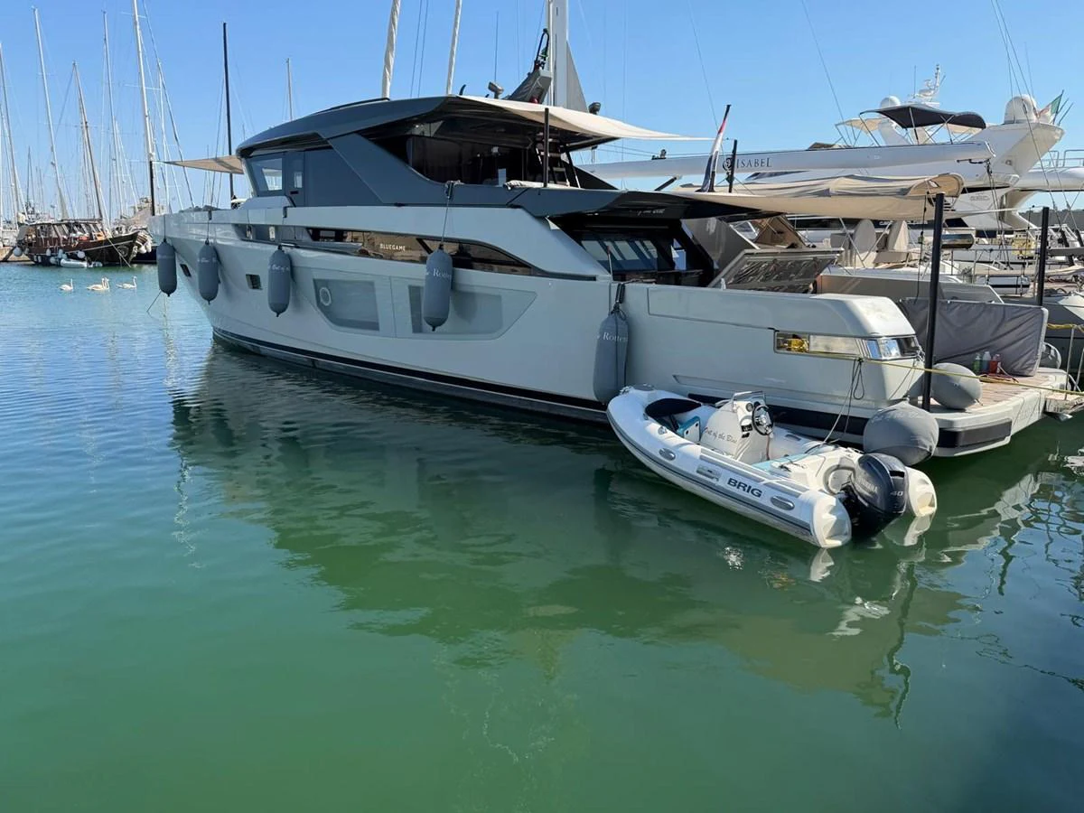 A sleek modern yacht is docked at a marina, accompanied by a small tender boat. aboard OUT OF THE BLUE Yacht for Sale