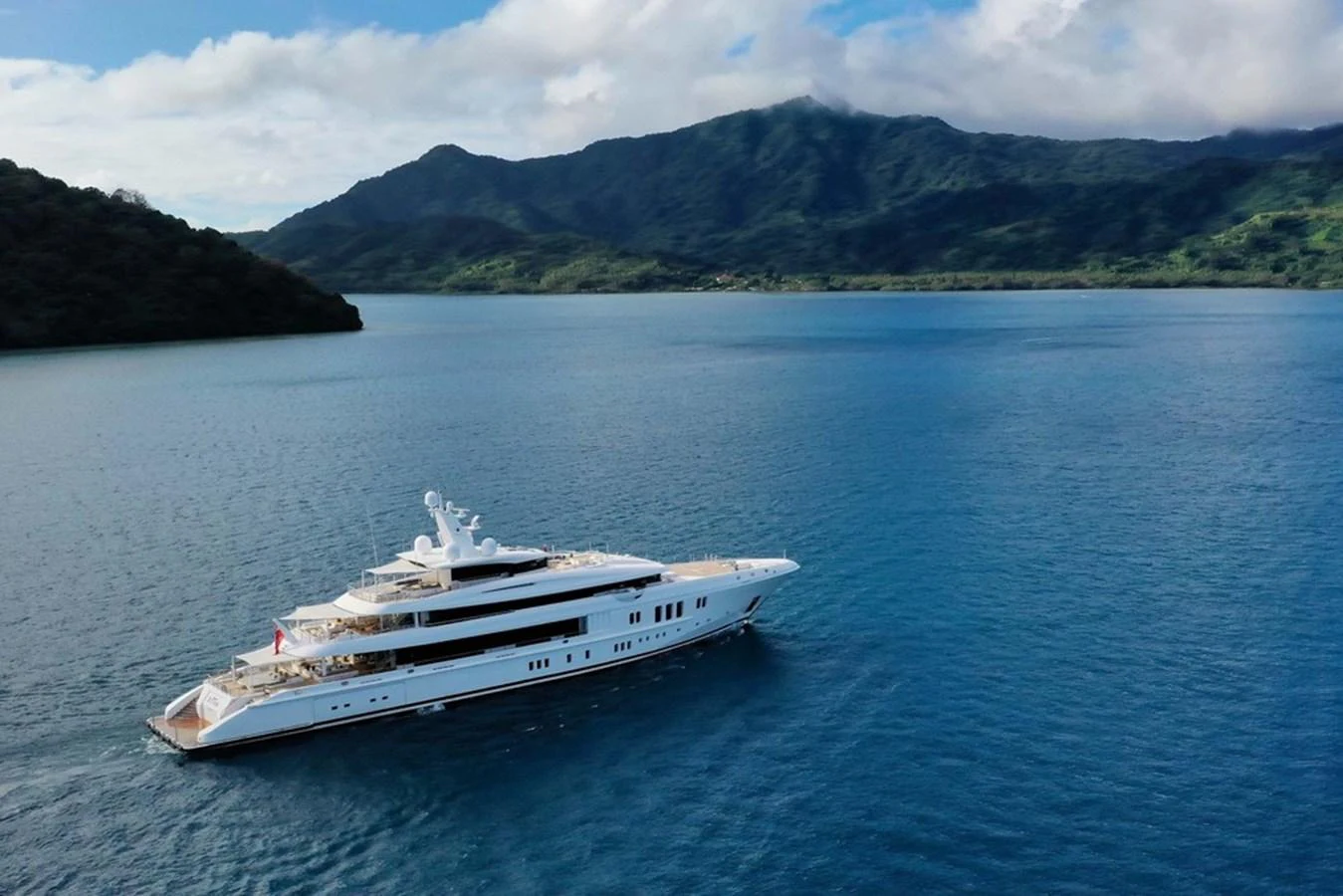 A sleek and luxurious yacht cruises through serene blue waters with a stunning mountainous backdrop. aboard DYTAN Yacht for Sale