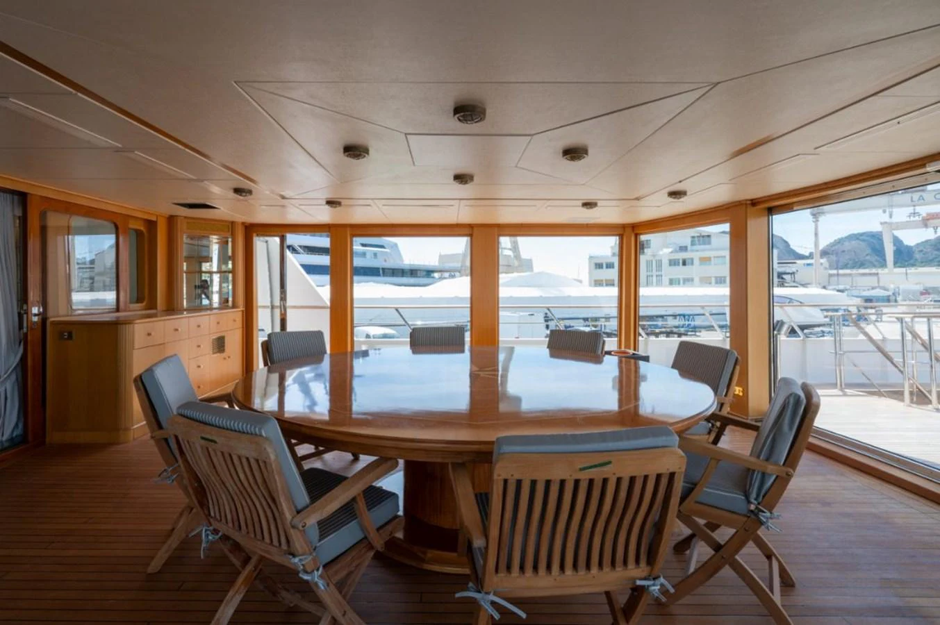 A spacious and elegant dining area with a large round table and comfortable chairs, offering a panoramic view of the marina. aboard STELLA FIERA II Yacht for Sale
