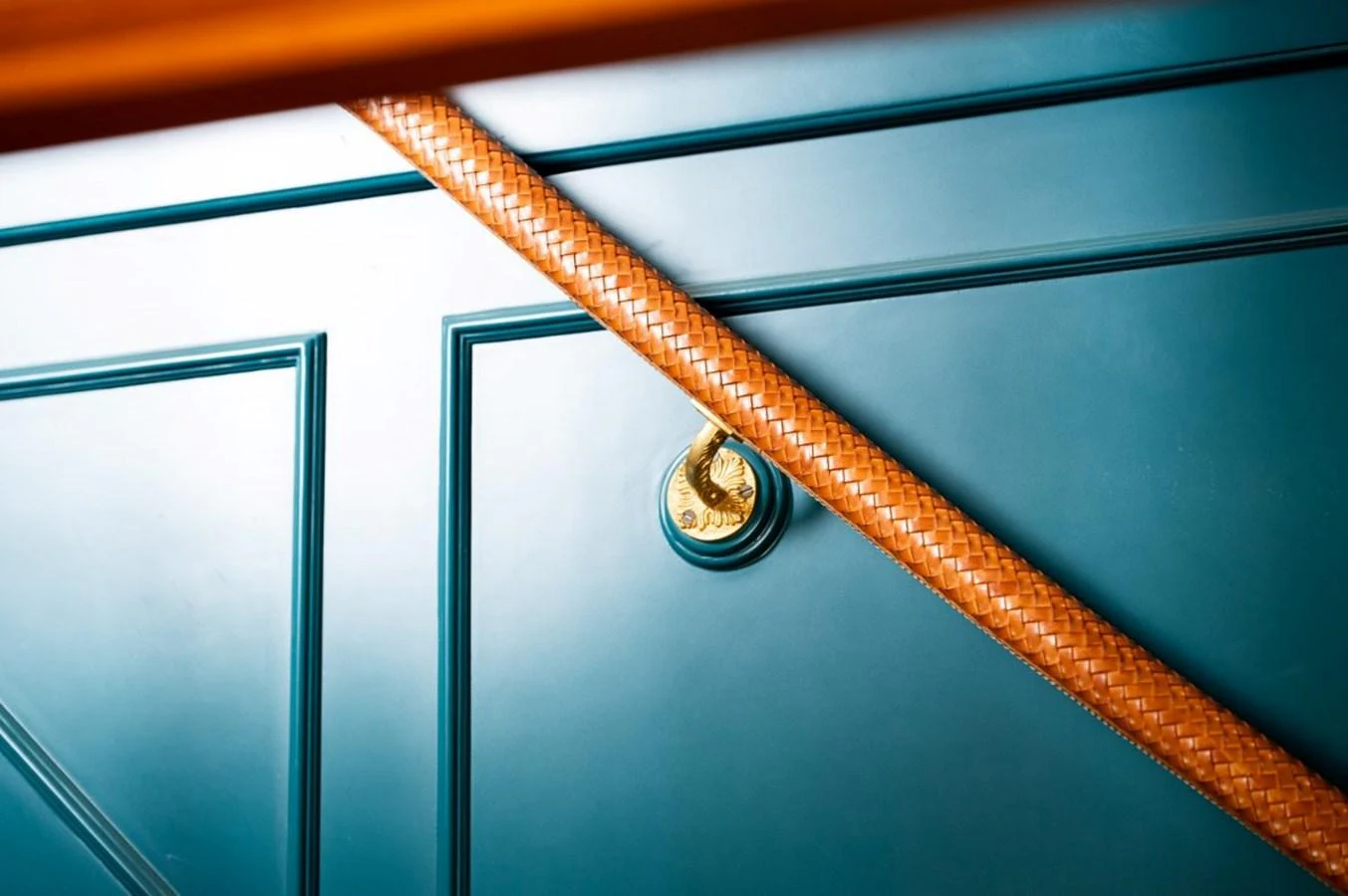 A close-up of a yacht's elegant blue paneling with a braided leather handrail and a brass fixture. aboard STELLA FIERA II Yacht for Sale