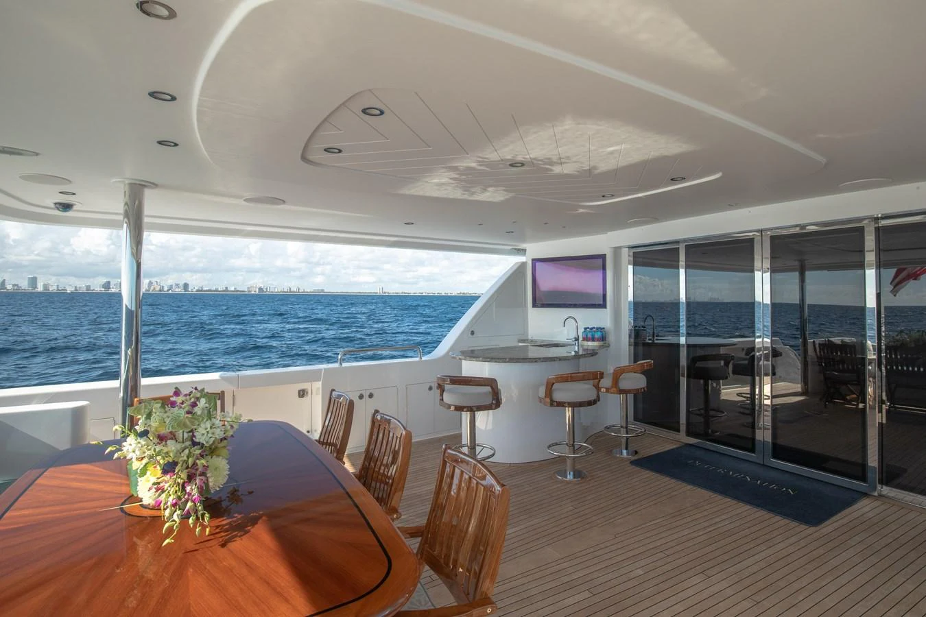 The aft deck features a spacious seating area with a dining table and bar stools, offering stunning ocean views. aboard DETERMINATION Yacht for Sale