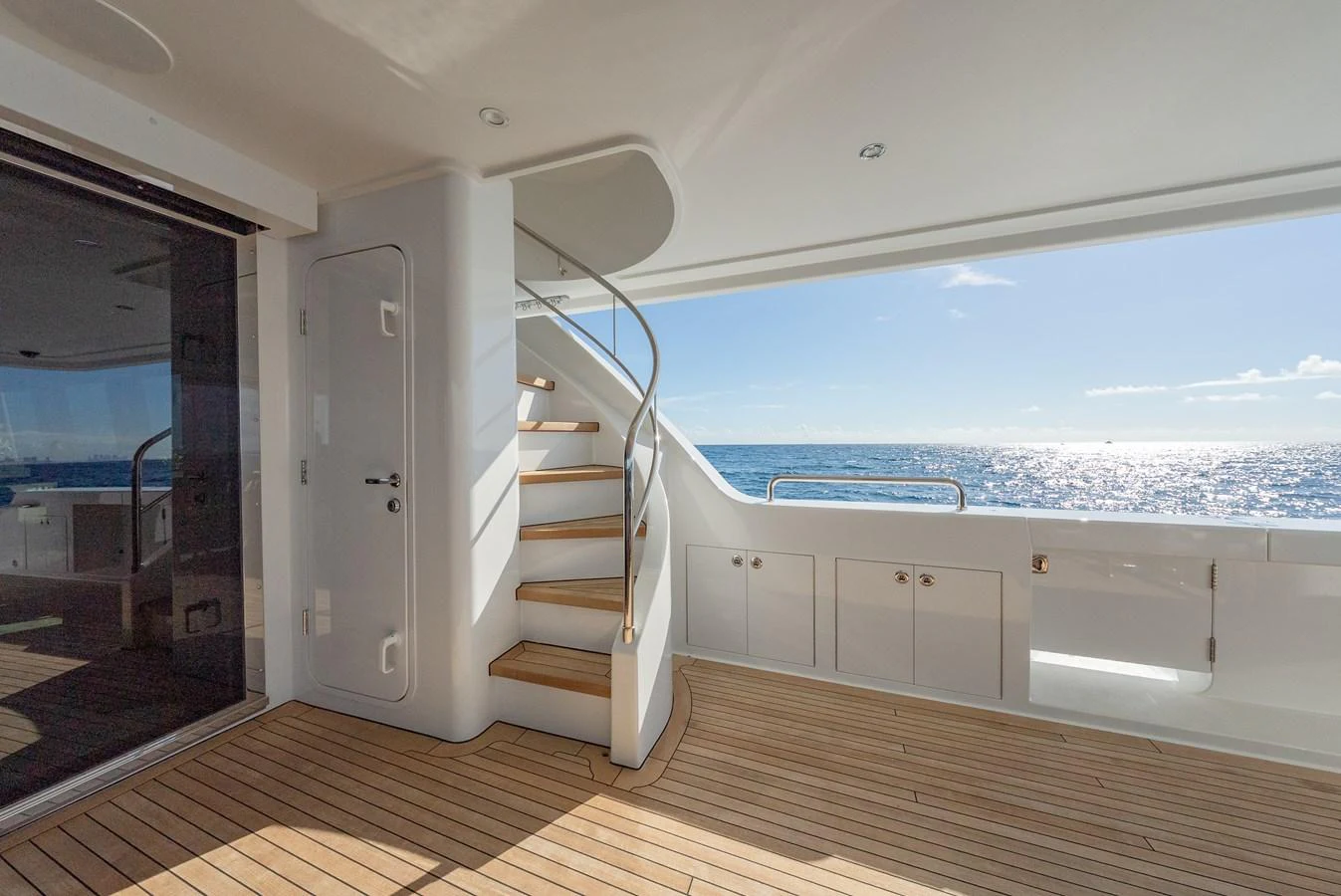 The aft deck features elegant wooden flooring and a spiral staircase leading to the upper deck, with a stunning ocean view. aboard DETERMINATION Yacht for Sale