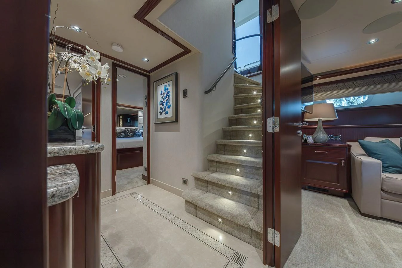 The interior features a luxurious staircase leading to different levels of the yacht, with elegant decor and ambient lighting. aboard DETERMINATION Yacht for Sale