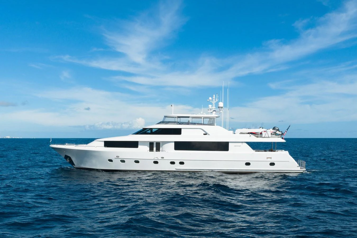 A sleek white yacht cruises gracefully on the open sea under a clear blue sky. aboard DETERMINATION Yacht for Sale