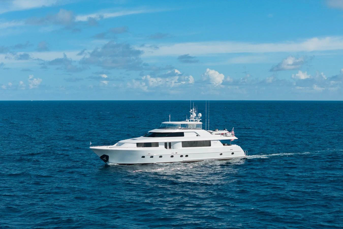 A sleek white yacht cruises through the open sea under a clear blue sky. aboard DETERMINATION Yacht for Sale