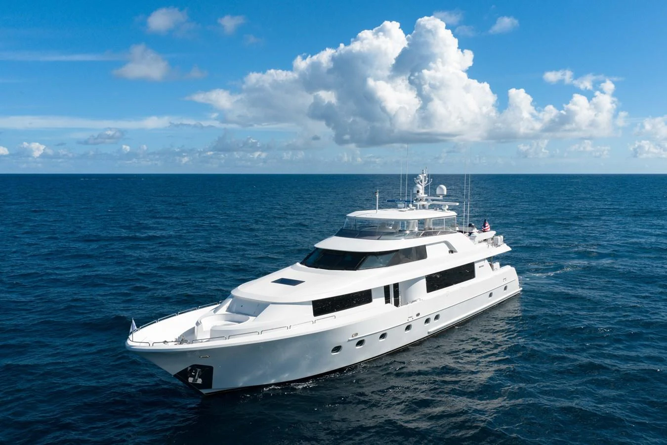 A luxurious white yacht cruises through the open sea under a bright blue sky with scattered clouds. aboard DETERMINATION Yacht for Sale