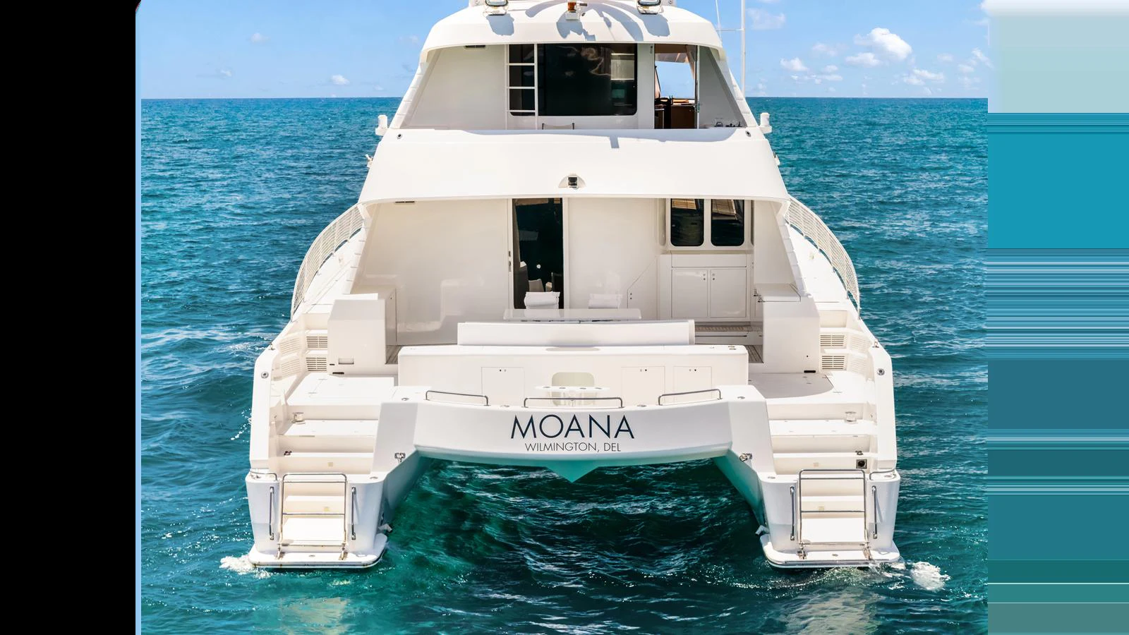 The yacht is seen from the rear, showcasing its spacious deck and sleek design against a beautiful ocean backdrop. aboard MOANA Yacht for Sale