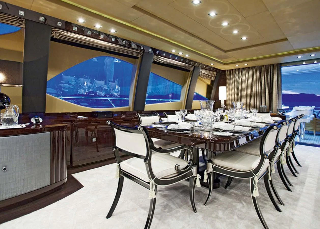 The yacht's dining area features an elegant table set for a formal meal, surrounded by luxurious seating and large windows offering stunning views. aboard RUSH Yacht for Sale