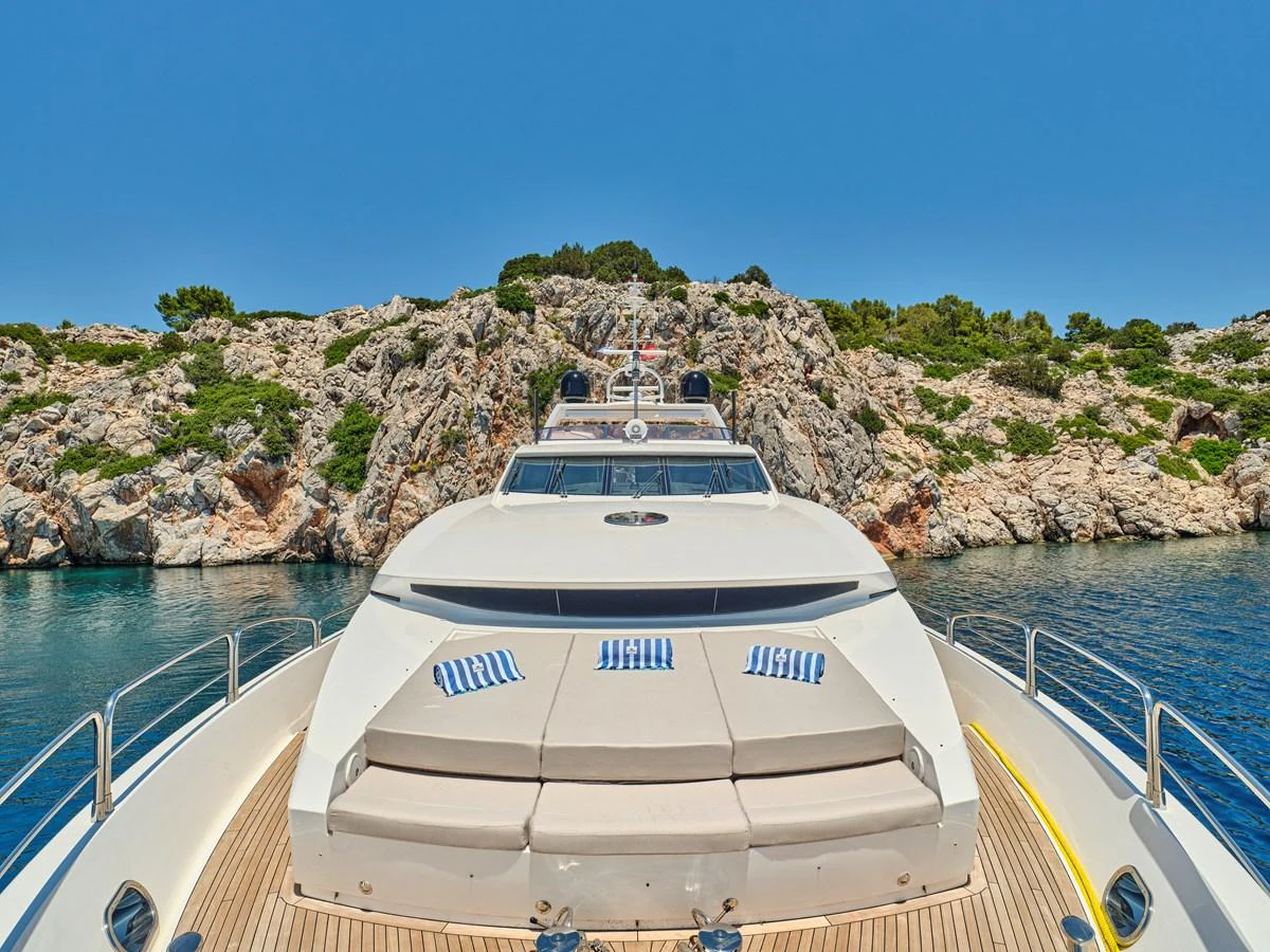 The yacht's foredeck offers a spacious sunbathing area with plush cushions, set against a stunning rocky coastal backdrop. aboard BLADE I Yacht for Sale