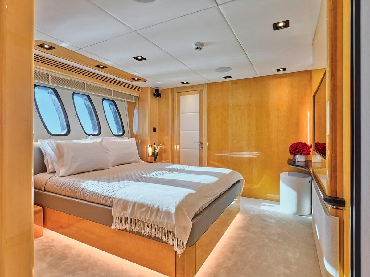 A luxurious stateroom featuring a large bed, warm wood paneling, and ample natural light. aboard BLADE I Yacht for Sale