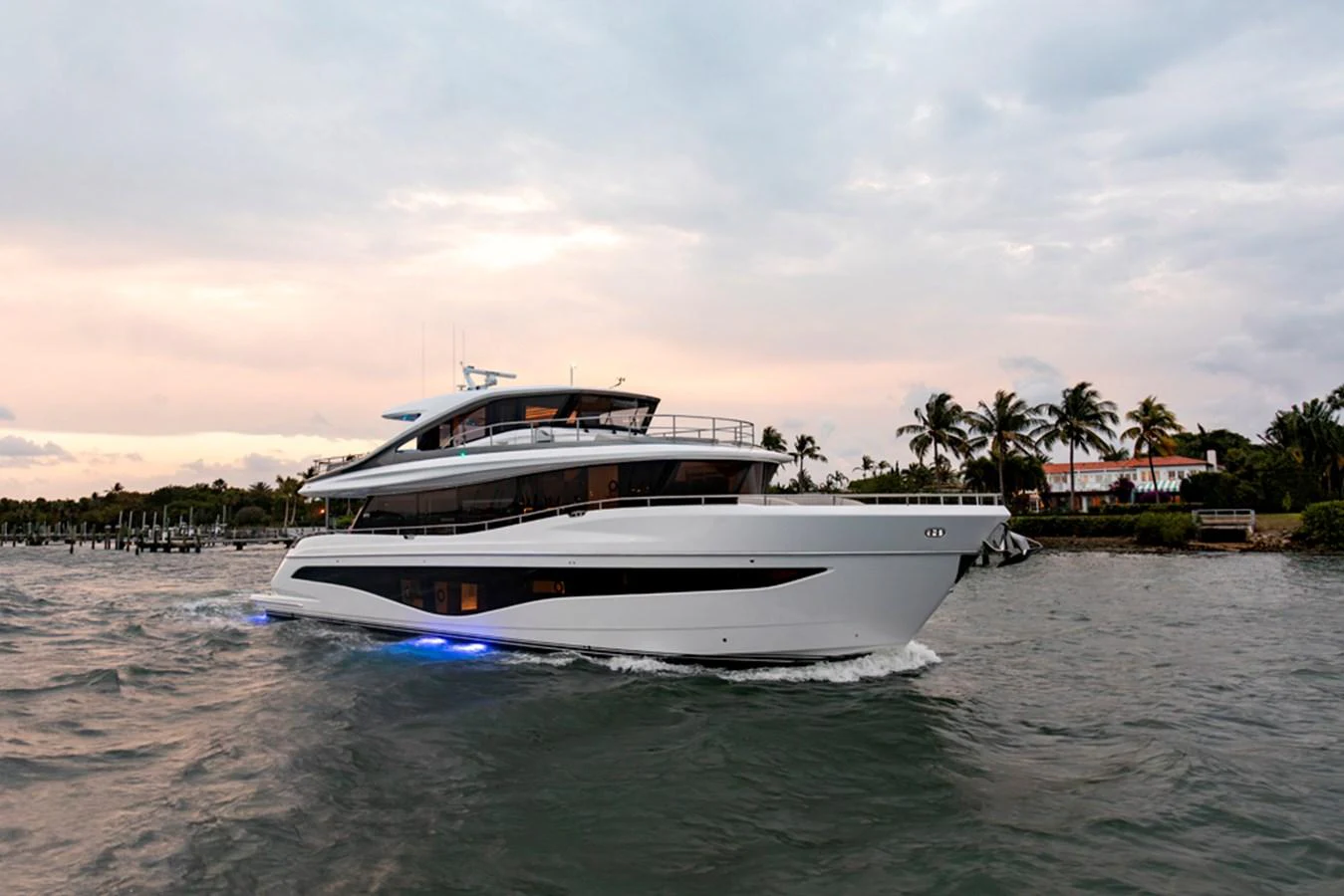 A sleek and modern yacht glides through the water at dusk, illuminated by subtle blue lights. aboard PRINCESS X80 Yacht for Sale
